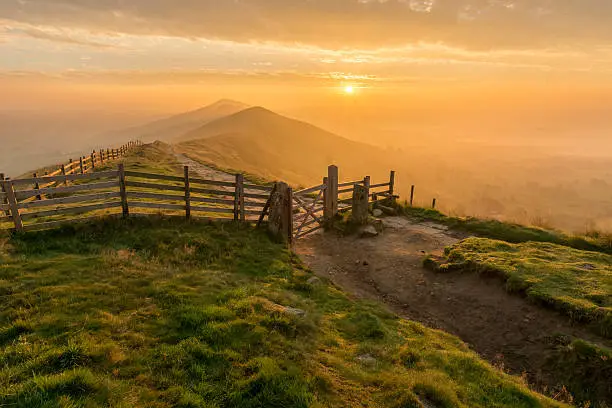 Golden sunrise at Mam Tor in the English Peak District on a hazy Autumn Morning with wooden gate.