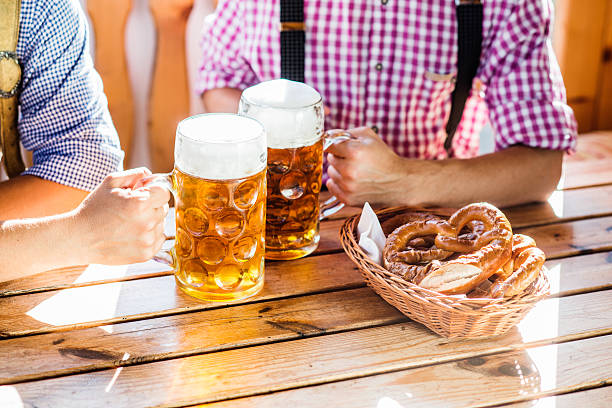 Man in traditional bavarian clothes holding mugs of beer Two unrecognizable men in traditional bavarian clothes sitting at the table, holding mugs of beer, clinking. Pretzels in basket. Beer Fest. oktoberfest beer stock pictures, royalty-free photos & images