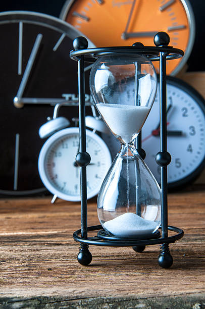 istock Hourglass and ticking clocks on old wooden table 600082370