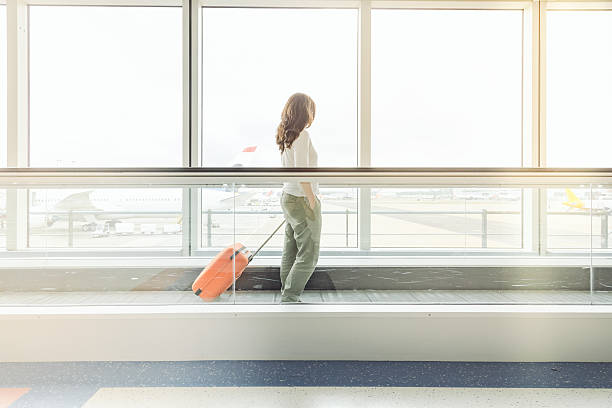 going to gate Young woman in an airport walking with trolley to the flight gate pedestrian walkway stock pictures, royalty-free photos & images