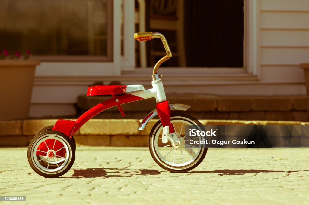 Child's rusted red tricycle standing ready Child's rusted favorite cherished red tricycle standing ready and waiting for its owner to arrive on paving outside a house Bicycle Stock Photo