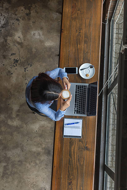 above view of woman having cappuccino while working with laptop - food currency breakfast business imagens e fotografias de stock