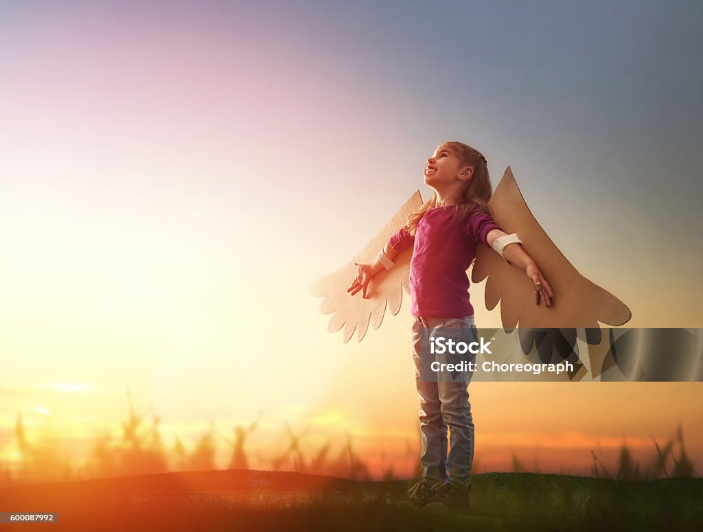 Kid with the wings of a bird Little girl plays outdoors. Child on the background of sunset sky. Kid with the wings of a bird dreams of flying. Child Stock Photo