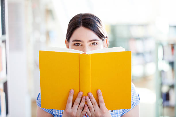 jeune femme lisant un livre dans la bibliothèque - book book cover healthcare and medicine medical exam photos et images de collection