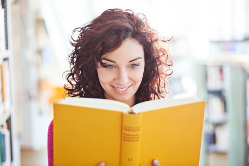 Portrait of young female reading a book at the library