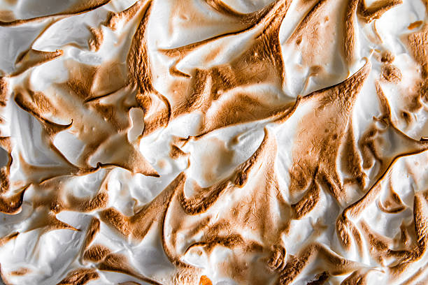 Homemade lemon meringue pie baked texture top view full frame Horizontal full frame composition monochrome color photography of close-up of part of beautiful homemade cooked lemon meringue pie, European cuisine tart with pastry dough, meringue white and brown texture making swirl, spiral and curve. This cake was taken from high angle view, top view unusual angle, view from above. Lemon meringue pie is a type of baked pie, usually served for dessert, made with a crust usually made of shortcrust pastry, lemon custard filling and a fluffy meringue topping. Lemon meringue pie is prepared with a bottom pie crust, with the meringue directly on top of the lemon filling. The cream is a mixture of eggs, sugar, lemon juice and lemon zest. Lemon flavored custards, puddings and pies have been enjoyed since Medieval times, but meringue was perfected in the 17th century. Lemon meringue pie, as it is known today, is a 19th-century product. The earliest recorded recipe was attributed to Alexander Frehse, a Swiss baker from Romandie. The lemon custard is usually prepared with egg yolks, lemon zest and juice, sugar, and, optionally, starch. The meringue, which includes well beaten egg whites and sugar, is cooked on top of the pie filling. As the meringue bakes, air bubbles trapped inside the protein of the egg whites will expand and swell. meringue stock pictures, royalty-free photos & images