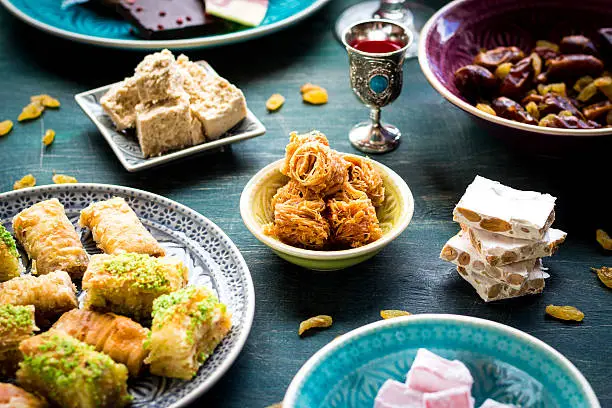 Set of assorted traditional eastern desserts. Arabian sweets on wooden table. Baklava, halva, rahat lokum, sherbet, nuts, pistachios, dates, raisins, kadayif in a colorful plates. Selective focus