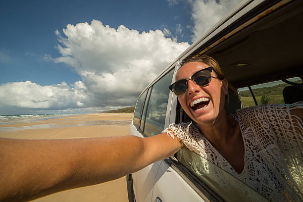 istock Young woman takes selfie while driving on sandy beach 600094130