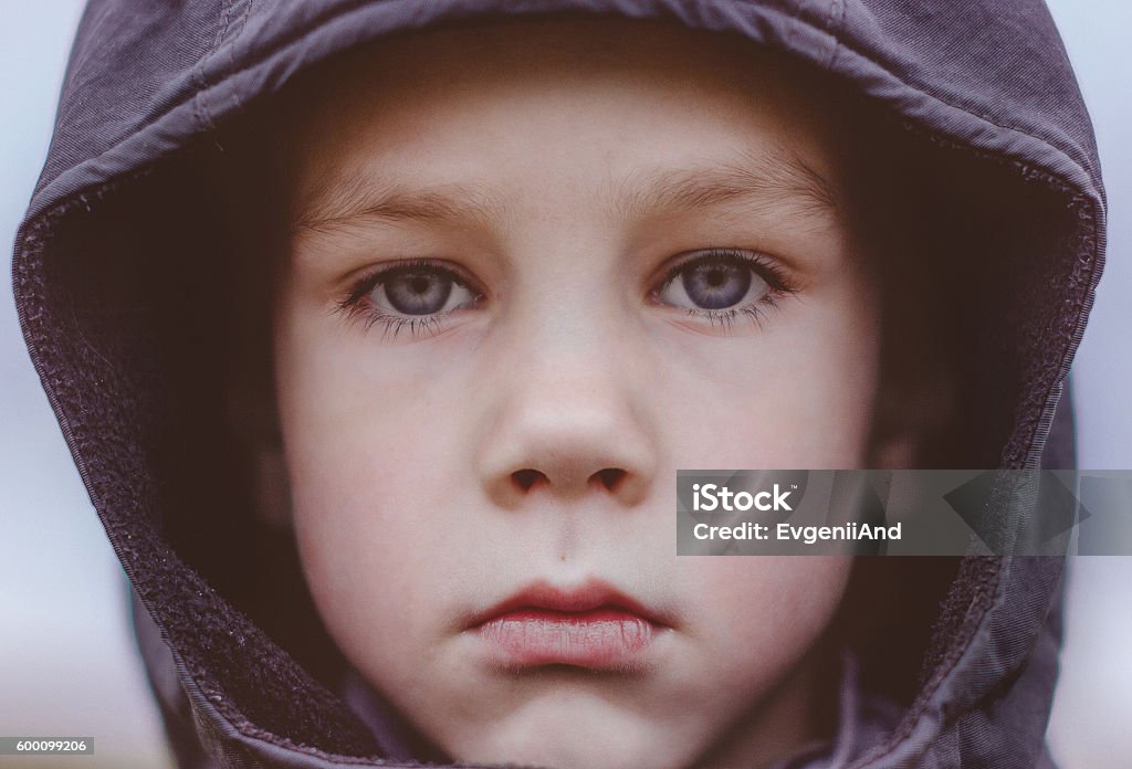 sad boy in a black hood. close-up kid with big blue eyes and long lashes sadly looking at the camera outdoors Child Stock Photo