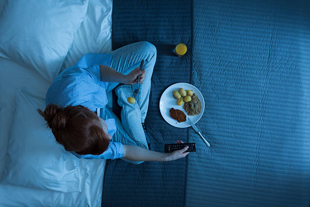 Woman and her life in a bed Photo from the top of young girl sitting on a bed, eating dinner and watching television evening meal stock pictures, royalty-free photos & images
