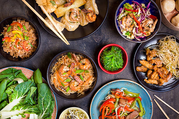 Chinese food on a dark table Chinese food on dark wooden table. Noodles, fried rice, dumplings, stir fry chicken, dim sum, spring rolls, bean sprouts, bok choy. Chinese cuisine set. Dinner party. Top view. Chinese restaurant asian food stock pictures, royalty-free photos & images