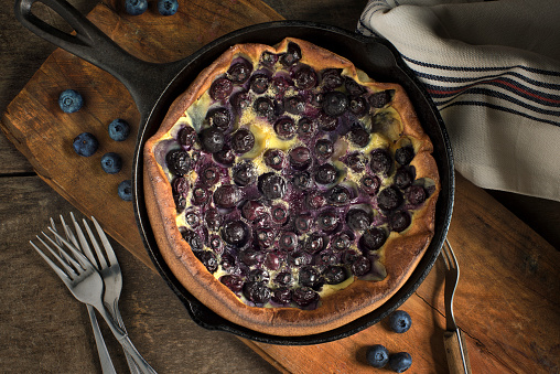 Blueberry clafoutis on rustic wood in an iron skillet shot from overhead