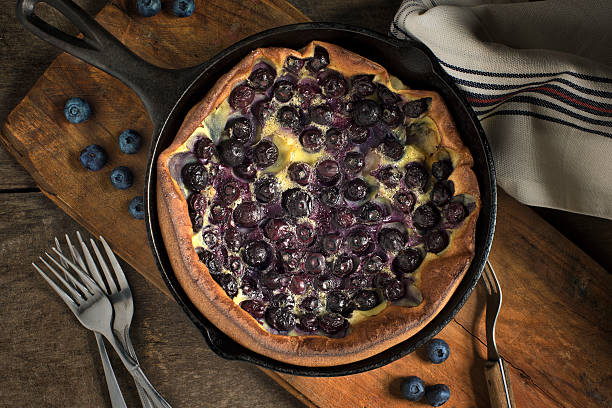 Blueberry Clafoutis Overhead view Blueberry clafoutis on rustic wood in an iron skillet shot from overhead clafoutis stock pictures, royalty-free photos & images