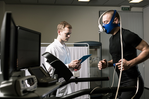 Athlete in oxygen mask running on treadmill and medic in white uniform