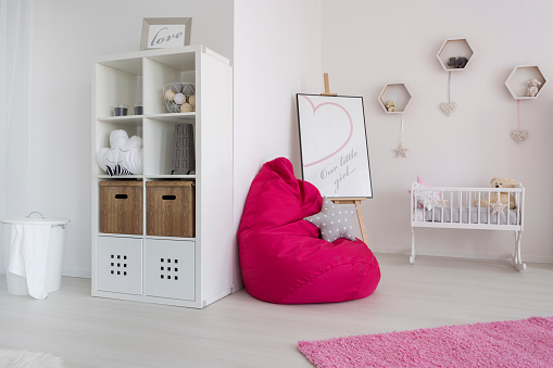 Fragment of a very bright newborn's room with a fuchsia sit sack next to a white cradle