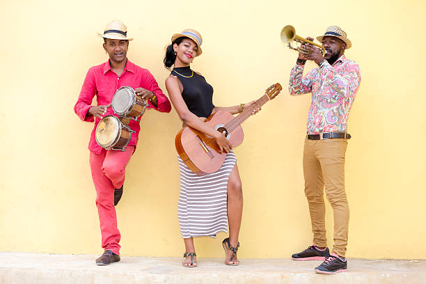Cuban Musical Band Cuban musical band, the trio consisting of a well known musicians standing against the bright yellow wall. Beautiful young woman standing in the middle, holding a guitar. The man on the left holding the small drums bongos, and a musician on the left holding a trumpet. Havana, Cuba, 50 megapixel image. salsa music photos stock pictures, royalty-free photos & images