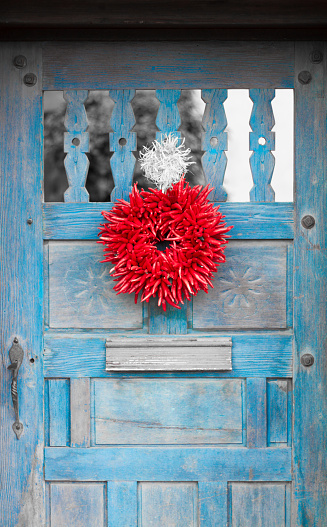 A red chili pepper ristra wreath hangs on a vintage blue door. A ristra is not only decorative in New Mexico but also protects a house from evil spirits according to traditional beliefs.