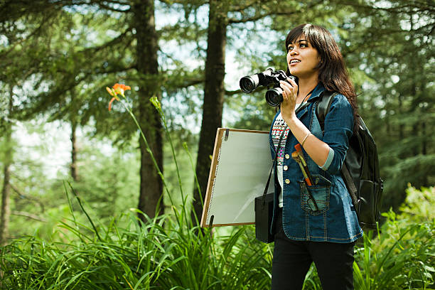 Artist with binocular, drawing board and art equipments searching subject.