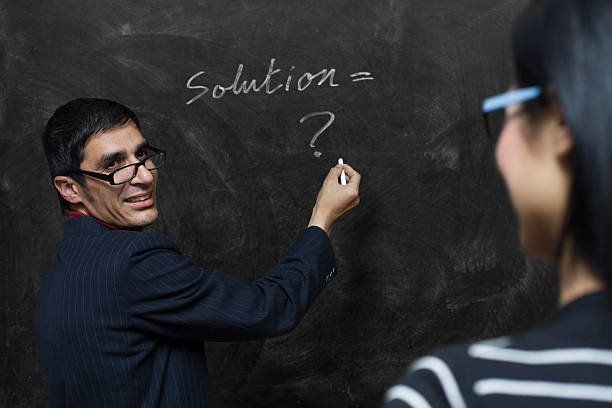 Teacher writing on blackboard and looking at his female student.