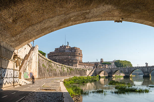 Rome, Italy - September 2, 2016: Cyclist has a ride alongside River Tiber near the famous Castel Sant'Angelo, a towering cylindrical building commissioned by the Roman Emperor Hadrian as a mausoleum for himself.