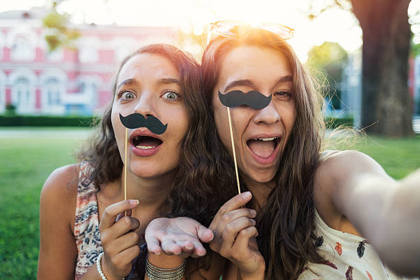 Girls making selfie with stache-on-a-stick Girls making selfie and having fun with stache-on-a-stick in the park women movember mustache facial hair stock pictures, royalty-free photos & images