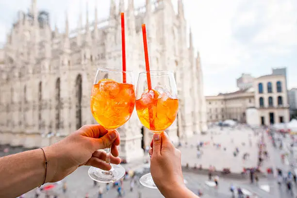 Clinking glasses of spritz aperol drink on the main square with Duomo cathedral on the background in Milan city