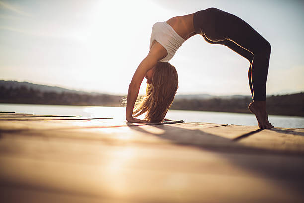 Beautiful young woman practicing yoga at lake