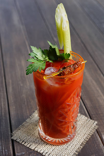 Bloody mary cocktail garnished with celery, popular alcohol drink Bloody mary cocktail garnished with celery, prune, onions, parsley and ice. Vodka and tomato juice in glass on wooden table closeup. Popular alcohol drink. bloody mary stock pictures, royalty-free photos & images