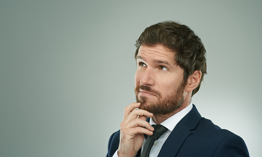 Studio shot of a thoughtful businessman standing with his hand on his chin against a grey background