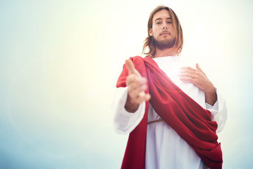 Shot of Jesus standing with his hand outstretched on a bare landscape