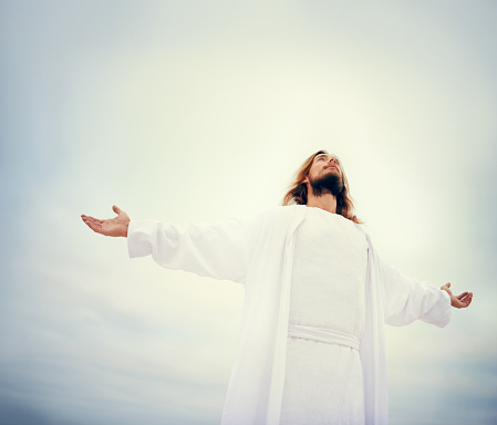Shot of Jesus standing with his arms outstretched on a bare landscape