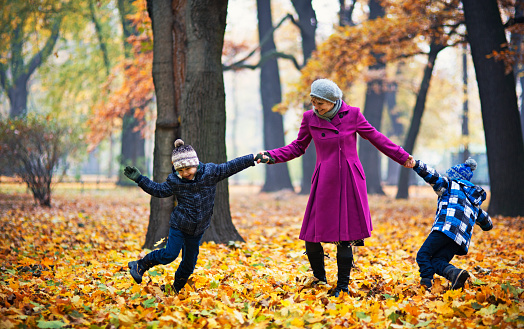 Little boys playing with their mother in an autumn park. The kids are laughing happily. Mother is spinning with the boys.