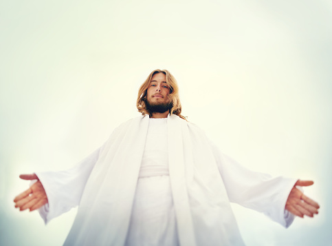 Shot of Jesus standing with his arms outstretched on a bare landscape