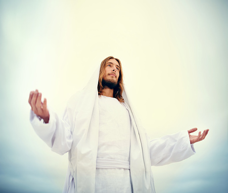 Shot of Jesus standing with his arms outstretched on a bare landscape