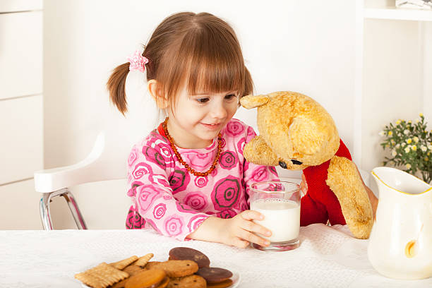 Cute little girl giving glass of milk to teddy bear stock photo