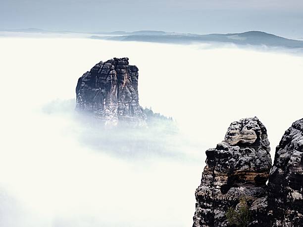 Sharp sandstone rock empire sticking out from heavy fog. Deep misty valley full of creamy mist. Popular climbers resort in autumn look