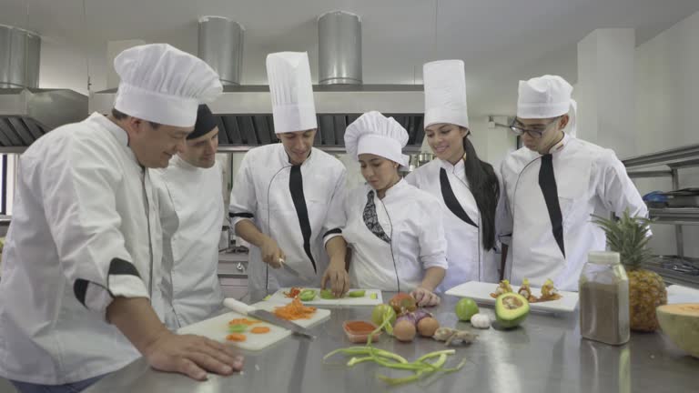 Chef observing his student focusing and chopping a tomato and the rest of the class also observing