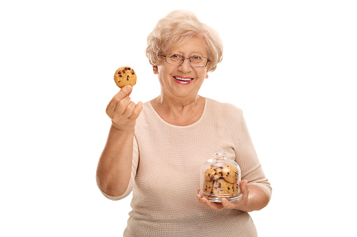 Happy mature woman holding a cookie and a jar full of cookies isolated on white background