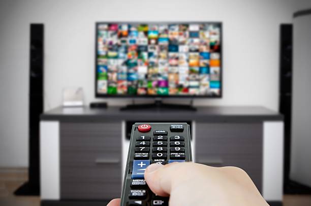 Watching television in modern TV room. Hand holding remote control