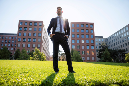 Low angle view of confident businessman standing on grassy field in city