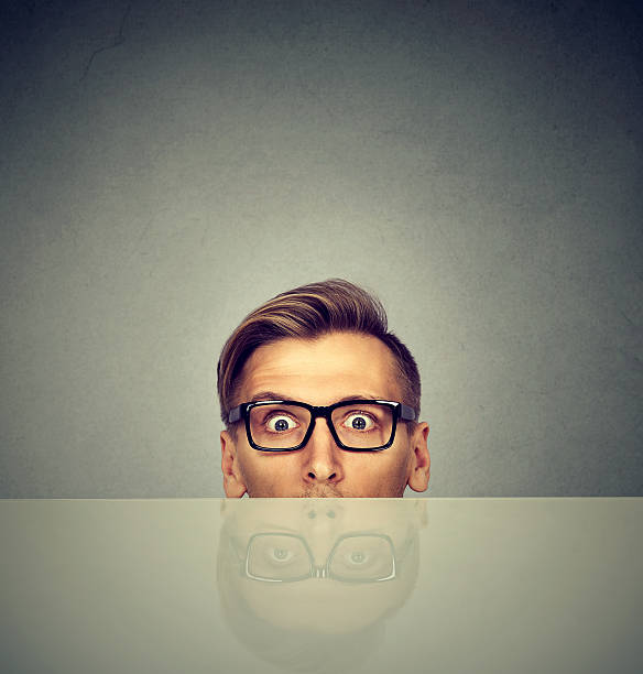 istock surprised businessman peeking from under the table 600384662