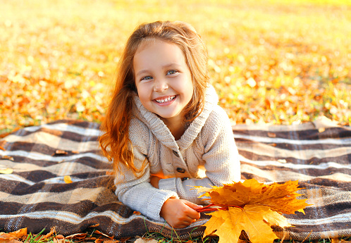 Portrait happy smiling child lying having fun with yellow maple leafs in sunny autumn day