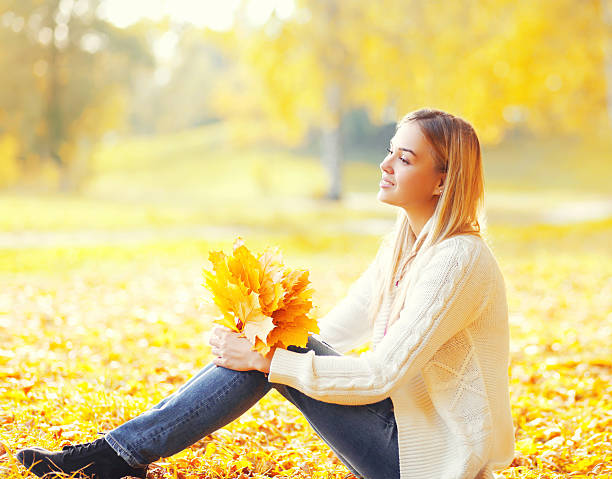 красивая молодая женщина сидит с желтыми кленовыми листьями осенью - cardigan стоковые фото и изображения