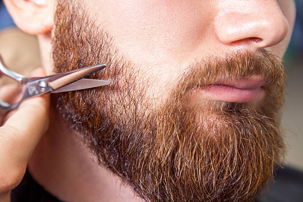 istock Barber with scissors shaving bearded man 600405336