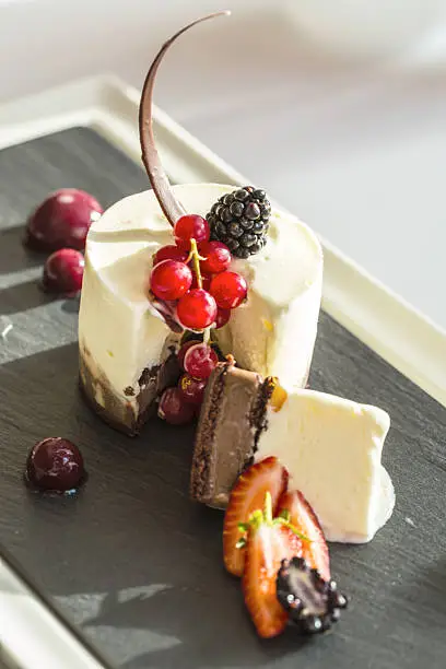 Trio of chocolate parfait with summer berries and sphere of blueberry served on a stone slate with white table cloth