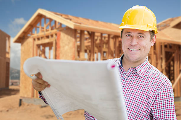 istock Contractor Wearing Hardhat Holding Blueprints at Construction Site 600412578