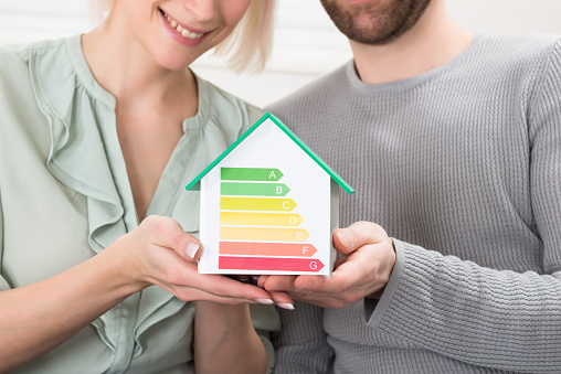 Close-up Of Young Couple Showing Energy Efficiency Rate On House Model At Home