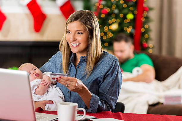 donna caucasica sorridente che tiene in braccio il bambino e acquista regali di natale online - christmas shopping internet family foto e immagini stock