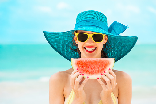 Happy woman enjoying a slice of watermelon on the beach.