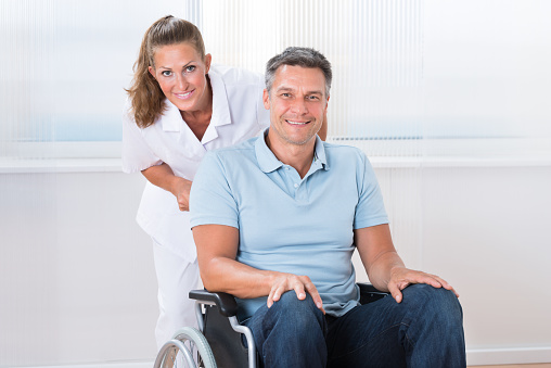 Happy Female Doctor Carrying Male Patient On Wheelchair